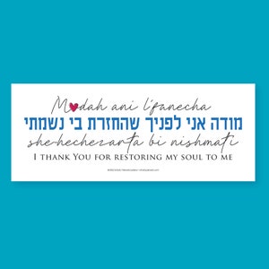 May include: A white rectangle with blue and black text that reads 'Modah ani l'panecha she-hechezarta bi nishmati' in Hebrew and English. The Hebrew text translates to 'I thank you for restoring my soul to me.' The text is in a handwritten font and there is a small red heart above the word 'Modah'.