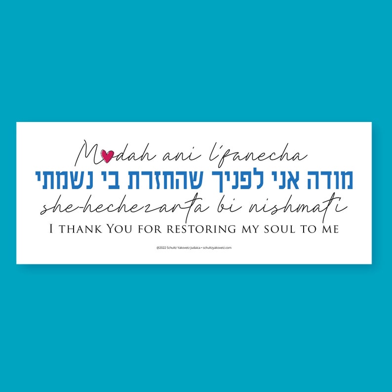 May include: A white rectangle with blue and black text that reads 'Modah ani l'panecha she-hechezarta bi nishmati' in Hebrew and English. The Hebrew text translates to 'I thank you for restoring my soul to me.' The text is in a handwritten font and there is a small red heart above the word 'Modah'.