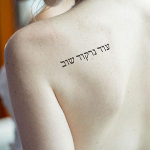 May include: A close-up of a person's back with a tattoo in Hebrew that reads "God is good".
