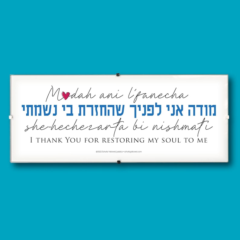 May include: A white sign with blue and black text that reads 'Modah ani l'panecha she hechezarta bi nishmati' which translates to 'I thank you for restoring my soul to me.' The sign also includes a small red heart.