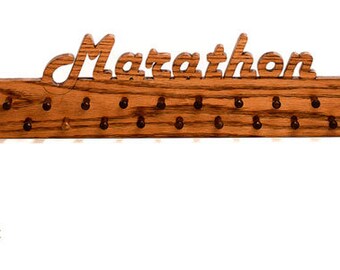 Könnte beinhalten: Marathon-Medaillen-Display aus Holz mit dunkelbraunem Walnuss-Finish. Das Wort "Marathon" ist oben ausgeschnitten. Es hat 21 Stifte zum Aufhängen von Medaillen. Die Holzmaserung ist sichtbar.