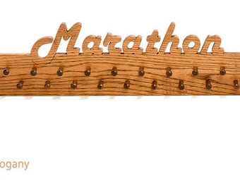Könnte beinhalten: Marathon-Medaillen-Display aus Holz mit dem Wort "Marathon" oben ausgeschnitten. Das Display ist goldmahagonifarben und hat 21 Stifte zum Aufhängen von Medaillen. Das Display ist aus Holz.