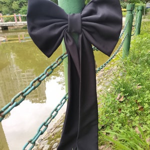 Peut inclure: Un grand nœud noir avec une longue queue, noué autour d'un poteau métallique vert. Le nœud est en tissu et a une finition lisse et brillante.