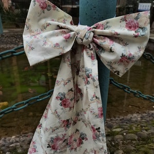 May include: A white fabric bow with a floral pattern in shades of pink and green, tied around a blue metal pole.