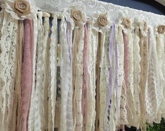 May include: A white lace curtain with burlap and pink ribbon accents. The curtain is made of multiple strands of lace and ribbon, and is decorated with burlap flowers.