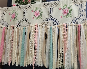 May include: A white crocheted curtain with pink and green fabric tassels. The curtain has a floral design with embroidered roses.