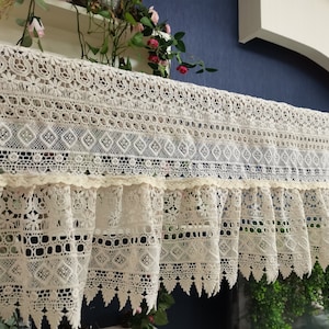 Puede incluir: Una cenefa de encaje blanco de ganchillo con un borde festoneado. La cenefa tiene un delicado patrón floral y un fondo con volantes.