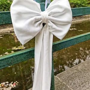May include: A large white satin bow tied around a green metal railing. The bow has a long tail that hangs down.