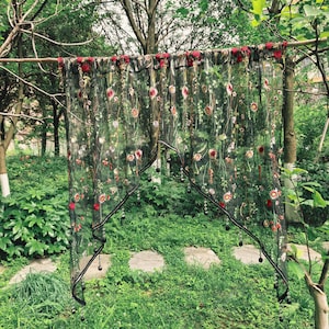 May include: A sheer black curtain panel featuring an intricate embroidered pattern of red, pink, and white flowers with green stems and leaves. The bottom edge is cut in a scalloped shape and adorned with small black beads hanging from the hem.