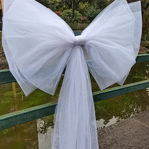 Peut inclure: Un grand nœud en tulle blanc noué autour d'une balustrade en métal. Le nœud est fait d'un tissu doux et transparent et a une longue queue flottante.