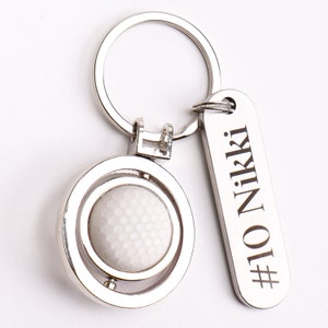 May include: Silver golf ball keychain with a spinning golf ball charm and a silver tag that says "#10 NIKKI".