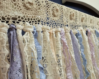May include: A decorative curtain made of crocheted lace with a fringe of various colors, including white, lavender, and blue.