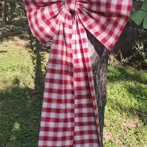 Puede incluir: Un gran lazo de cuadros rojos y blancos atado alrededor del tronco de un árbol. El lazo está hecho de tela y tiene una cola larga.