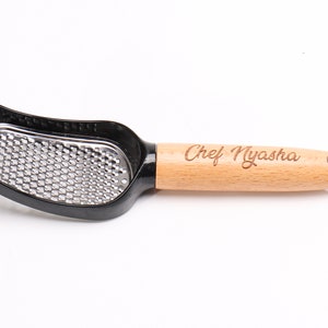 May include: A black and silver grater with a wooden handle. The handle is engraved with the text "Chef Nyasha".