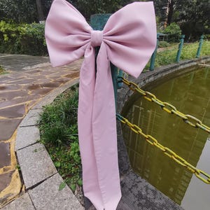 May include: A large pink satin bow with long tails tied around a wooden post. The bow is tied in a classic style with the tails hanging down.
