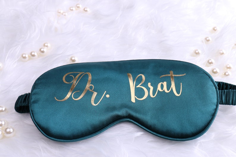 May include: A teal blue sleep mask with gold lettering that says "Dr. Brat".
