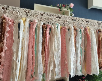 May include: A decorative banner made of crocheted lace and fabric ribbons in various shades of pink, white, and green. The banner is adorned with gold sequins.
