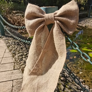 Könnte beinhalten: Ein großer, rustikaler brauner Juteschleife, die um einen Metallpfosten gebunden ist. Die Schleife besteht aus natürlichem Jutegewebe und hat ein schlichtes, elegantes Design.