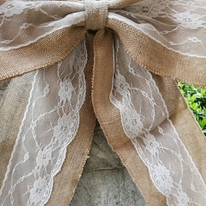 Op de afbeelding: Een grote jute strik met witte kant. De strik is om een houten paal gebonden.