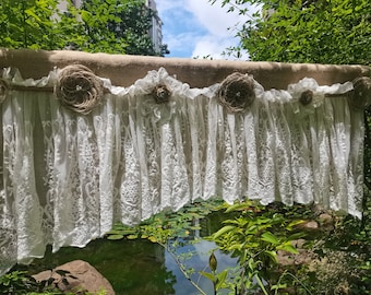May include: A white lace curtain valance with burlap flowers and a brown burlap backing. The valance is hanging in front of a pond with lily pads.