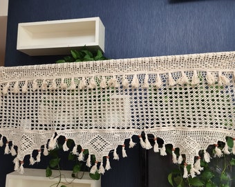 May include: A white crocheted valance with a geometric pattern and fringe trim. The valance has a scalloped bottom edge and wooden beads.