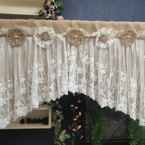 May include: A decorative valance featuring a burlap top with jute rope and floral accents. The white lace curtain has a floral pattern. The valance is adorned with jute and lace flower embellishments, adding a rustic touch to home decor.