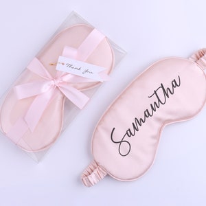 May include: A pale pink satin sleep mask with the name "Samantha" in black script. The mask has an elasticated band. A matching mask is in a clear box, tied with a pink ribbon and a "Thank you" tag.
