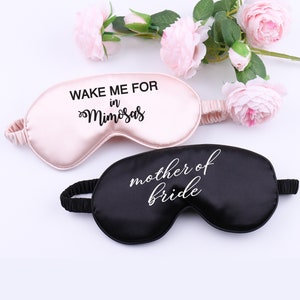 May include: Two satin sleep masks. One is pink with the text "Wake me for mimosas" in black. The other is black with the text "mother of bride" in white.