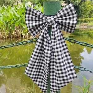 May include: A black and white gingham bow tied around a green post. The bow is tied in a large knot and the tails are long and flowing.
