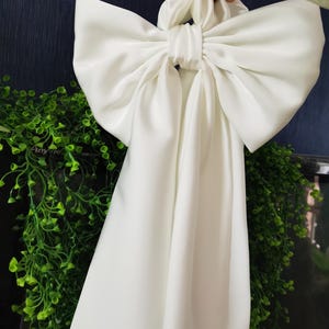 Peut inclure: Un grand nœud en satin blanc avec de longues queues. Le nœud est noué et les queues pendent.
