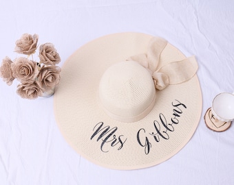 May include: A wide-brimmed straw sun hat with a large bow and the text "Mrs. Gibbons" embroidered in black.