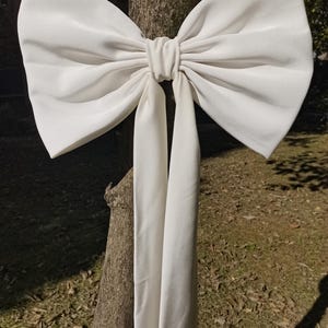 May include: A large white satin bow tied around a tree trunk. The bow has long tails that hang down.