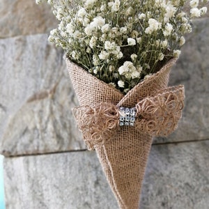 Puede incluir: Un ramo de aliento de bebé blanco arreglado en un cono de arpillera con un lazo de arpillera y un adorno de pedrería.