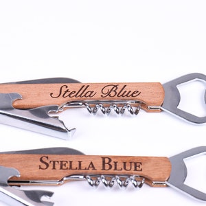 Puede incluir: Un abridor de botellas de madera con un sacacorchos y un abridor de tapas. El mango est&aacute; grabado con el nombre "Stella Blue".