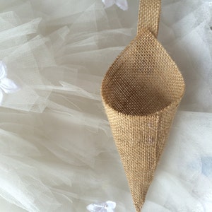 May include: A small, brown burlap cone-shaped bag with a handle. The bag is sitting on a white tulle fabric.