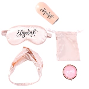 May include: A pink satin sleep mask, headband, and pouch with the name "Elizabeth" embroidered on them. A pink compact mirror with the same name is also included.