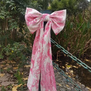 May include: A large pink bow with a white floral pattern tied around a metal post. The bow is made of fabric and has a long tail.