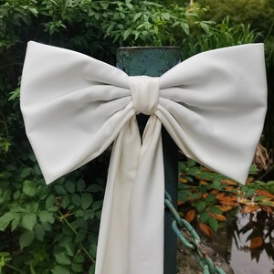 Peut inclure: Un grand nœud en satin blanc noué autour d'un poteau métallique. Le nœud est noué avec une longue queue qui pend le long du poteau.