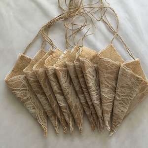 Op de afbeelding: Een set van 10 jute kegels met kantversiering, aan elkaar gebonden met touw. De kegels zijn lichtbruin van kleur en de kant is wit.