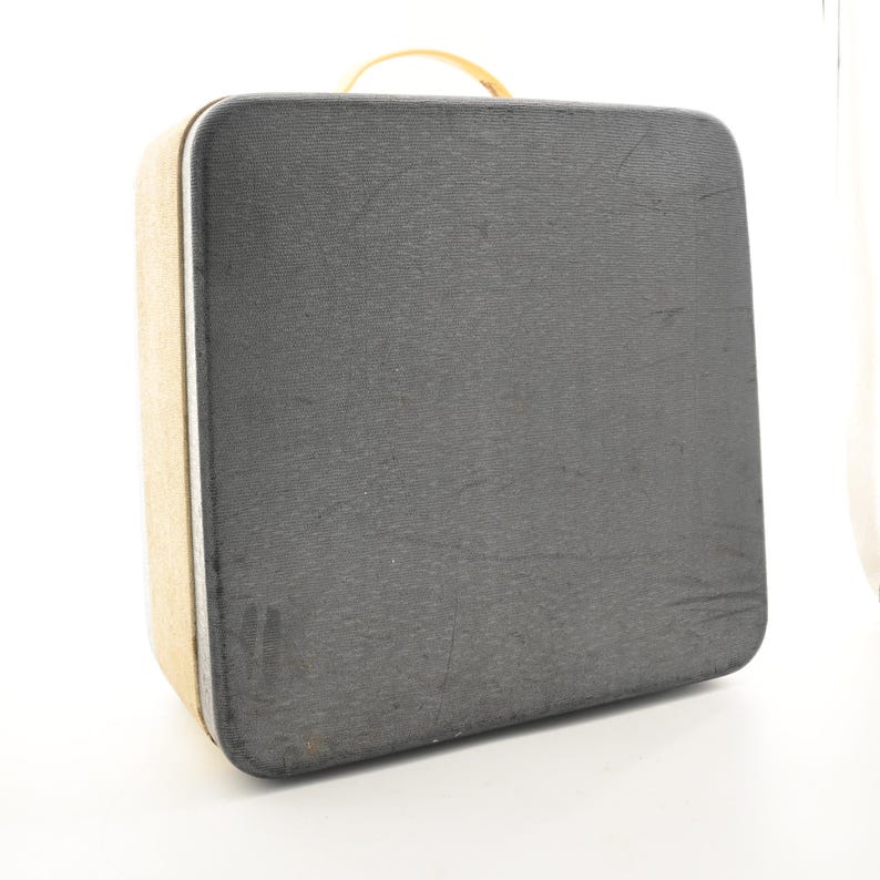 May include: A rectangular suitcase with a dark gray textured exterior and a light tan side panel. The suitcase features a rounded top handle and a silver-toned trim running along the edge of the case, providing a structured and functional design.