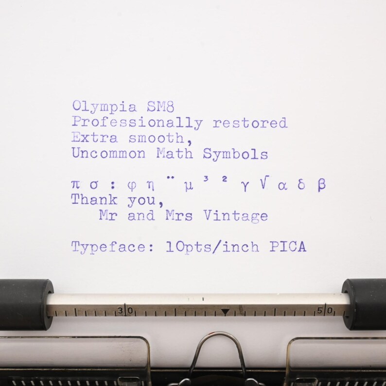 May include: A white sheet of paper in a typewriter with blue ink text reading Olympia SM8, Professionally restored, Extra smooth, Uncommon Math Symbols, various Greek and math characters, Thank you, Mr and Mrs Vintage, Typeface: 10pts/inch PICA.