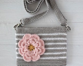 May include: A gray and white striped crocheted crossbody bag with a pink crocheted flower on the front. The bag has a long gray crocheted strap.