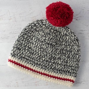 Może przedstawiać: Szary i biały wełniany beret z czerwonym pomponem na górze. Beret ma czerwoną i białą wstążkę wokół dołu.