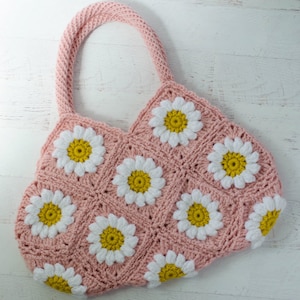 May include: A pink crocheted tote bag with white and yellow daisy flowers. The bag has two straps and is made with a granny square stitch.