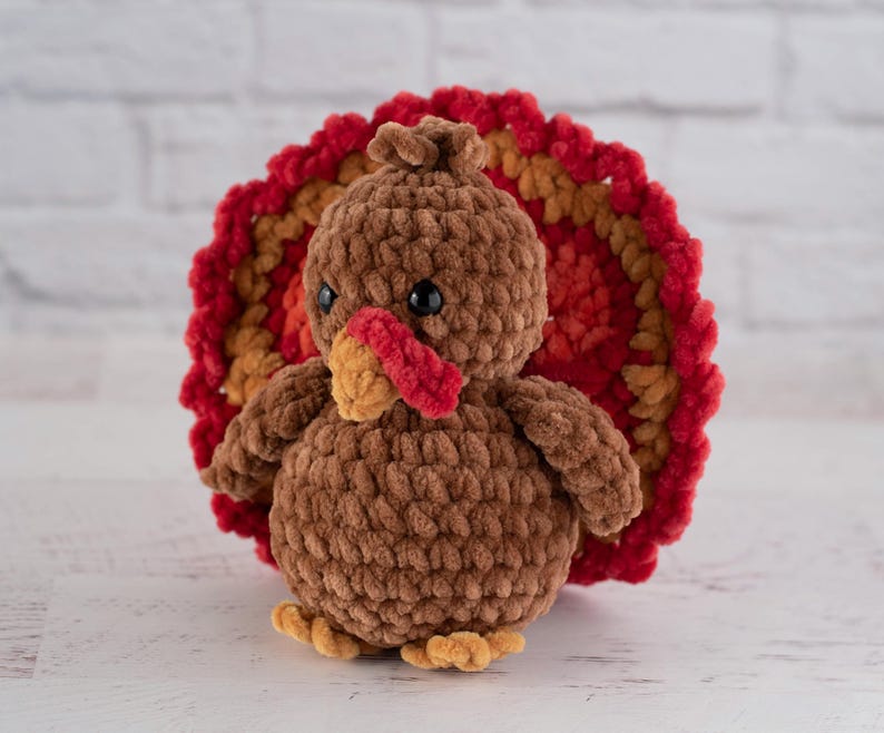 May include: A brown crocheted turkey with a red, orange, and yellow crocheted fan-shaped tail.