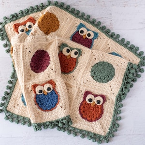 May include: A cream-colored crochet blanket featuring owl and circle designs. The blanket has a green pom-pom trim and is made of squares. The owls are in various colors, including blue, orange, and burgundy.