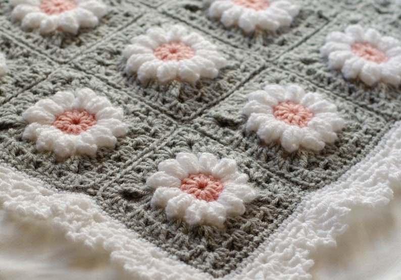 May include: A gray crocheted baby blanket with a white crocheted border and a pattern of pink and white flowers.