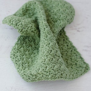 May include: A green crocheted dishcloth or kitchen towel. The cloth is made with a simple stitch pattern and has a soft, textured surface.