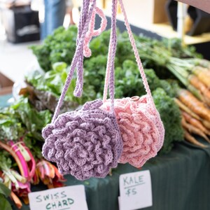 May include: Two small, round, crocheted bags with long straps. One bag is light purple and the other is light pink. Both bags feature a textured, layered petal design on the front, resembling a flower or succulent, and have a single button closure.