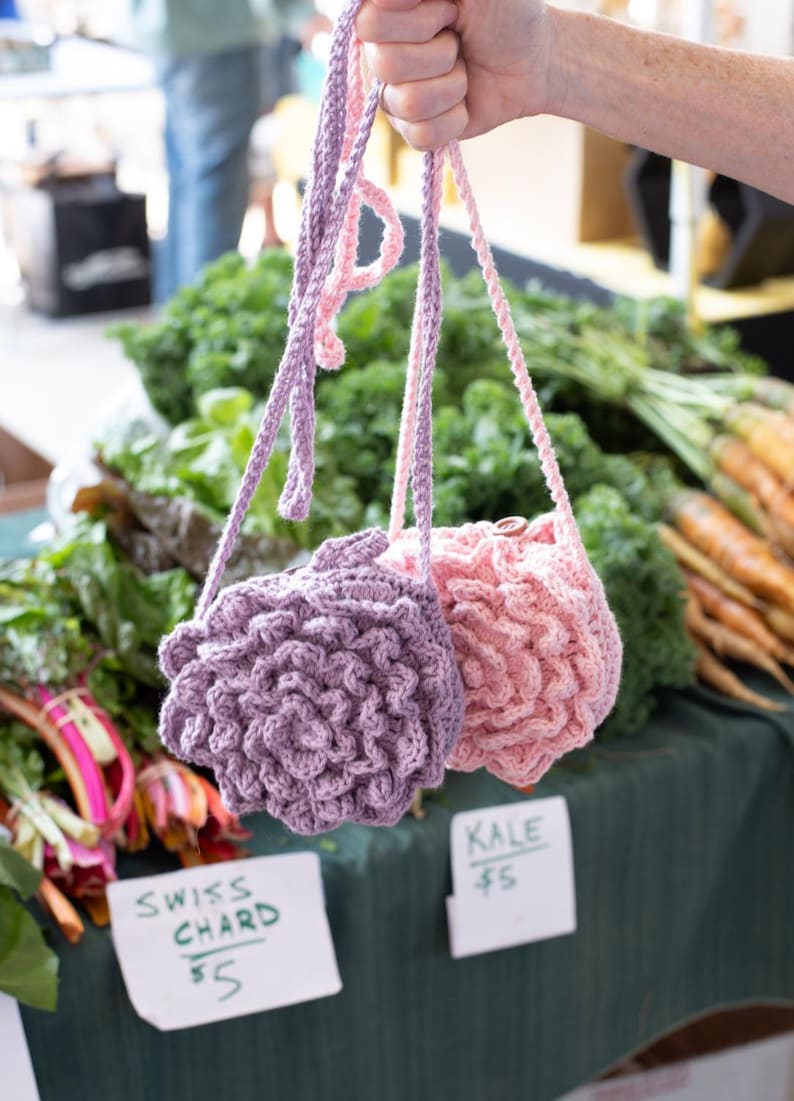 May include: Two small, round, crocheted bags with long straps. One bag is light purple and the other is light pink. Both bags feature a textured, layered petal design on the front, resembling a flower or succulent, and have a single button closure.